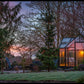 Exaco Janssens T-Shaped Royal Victorian Orangerie glowing at dusk in a wooded backyard