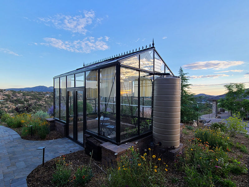 Royal Victorian VI36 greenhouse at sunset on a brick base with a rain barrel, garden path and hills behind