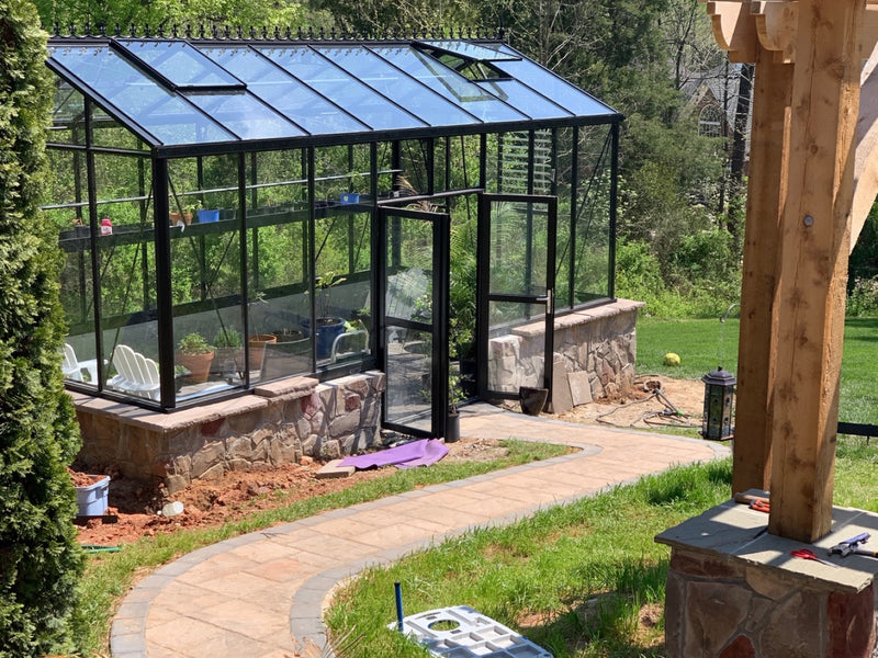 Royal Victorian VI34 greenhouse on a stone knee wall with double doors open and a curved paver path