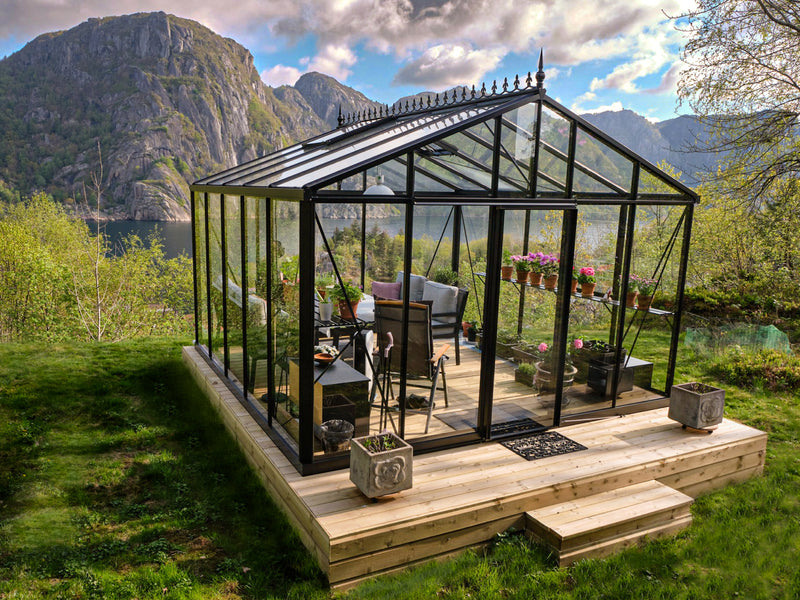 Royal Victorian VI34 greenhouse on a raised wooden deck with steps, furnished with seating and flowers