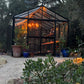 Customer photo: black Royal Victorian VI34 glass greenhouse at dusk, lit by a chandelier inside, on a gravel garden path