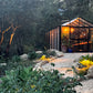Customer photo: black Royal Victorian VI34 greenhouse glowing at twilight at the end of a gravel path in a landscaped garden