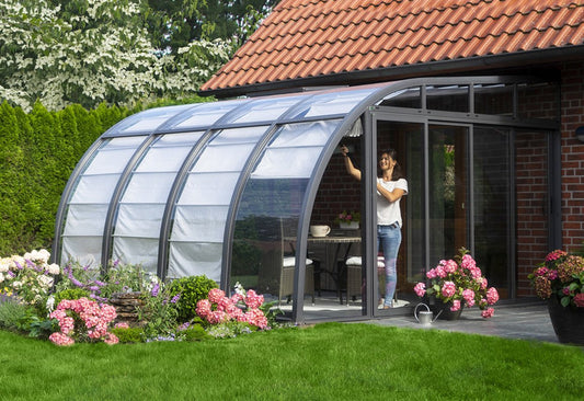 Hoklartherm Berlin Solarveranda lean-to sunroom with an anthracite frame and curved roof attached to a brick house, sliding front panels and pink hydrangeas