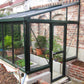 Black Janssens Arcadia lean-to glass greenhouse against a brick garden wall, door open