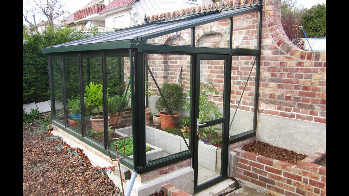 Black Janssens Arcadia lean-to glass greenhouse against a brick garden wall, door open