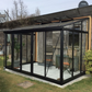 Black Janssens Arcadia lean-to greenhouse with sliding doors beside a garden building