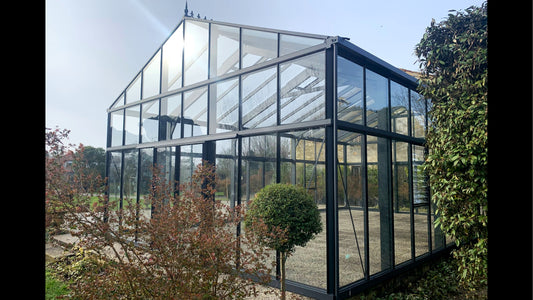 Black Janssens Gigant glass greenhouse in a garden setting