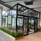 Janssens Modern greenhouse displayed in a showroom with planters (10x15 M34 shown)