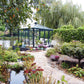 Janssens Pyramid glass greenhouse with black frame beside a pond in a landscaped garden