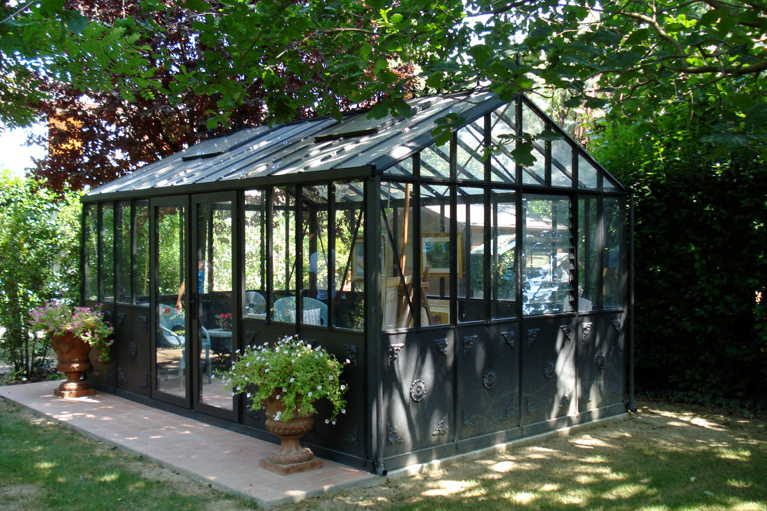 Janssens Retro Royal Victorian glass greenhouse in black, set in a landscaped garden