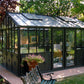 Larger model shown – black Retro Royal Victorian greenhouse on a tree-lined patio
