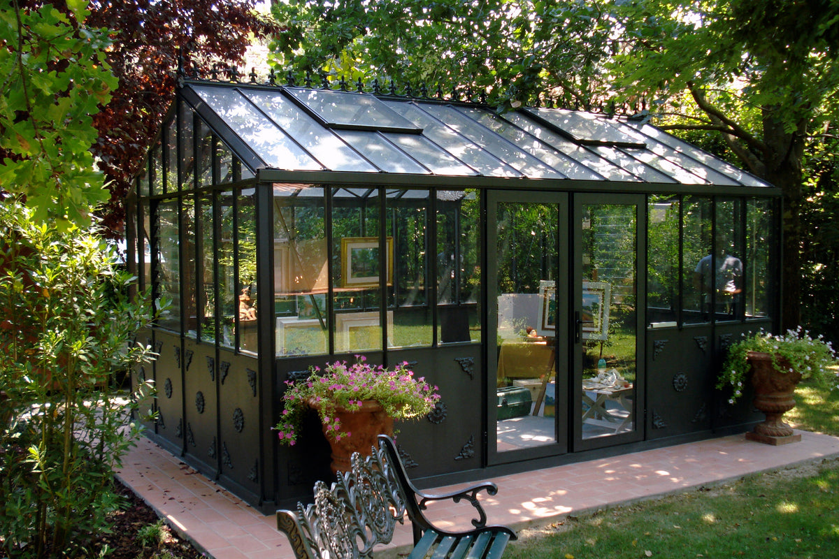 Larger model shown – black Retro Royal Victorian greenhouse on a tree-lined patio