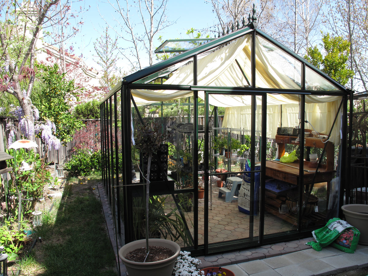 Larger model shown – Exaco Janssens Royal Victorian glass greenhouse in a garden with shade curtains