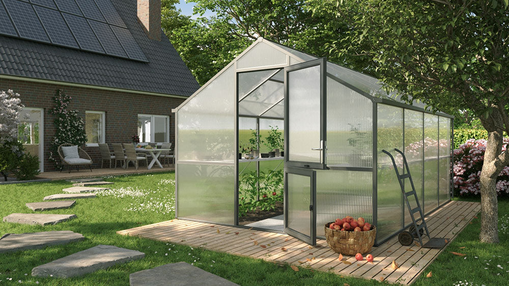 Nelke 4 Pro polycarbonate greenhouse on a wooden deck beside a brick house and apple tree