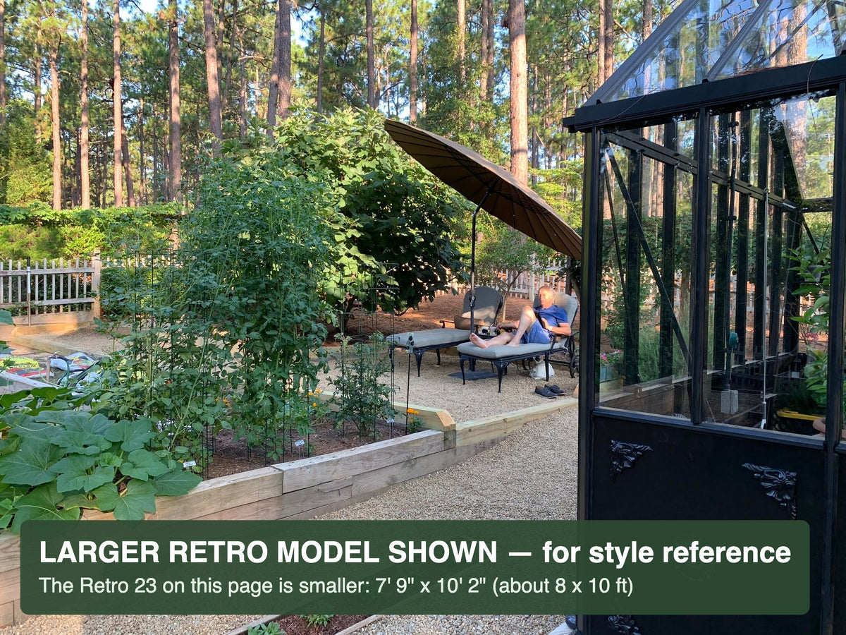 Garden view from the door of a black Janssens Retro Victorian greenhouse – larger Retro model shown for style reference; the Retro 23 is 7'9" x 10'2"