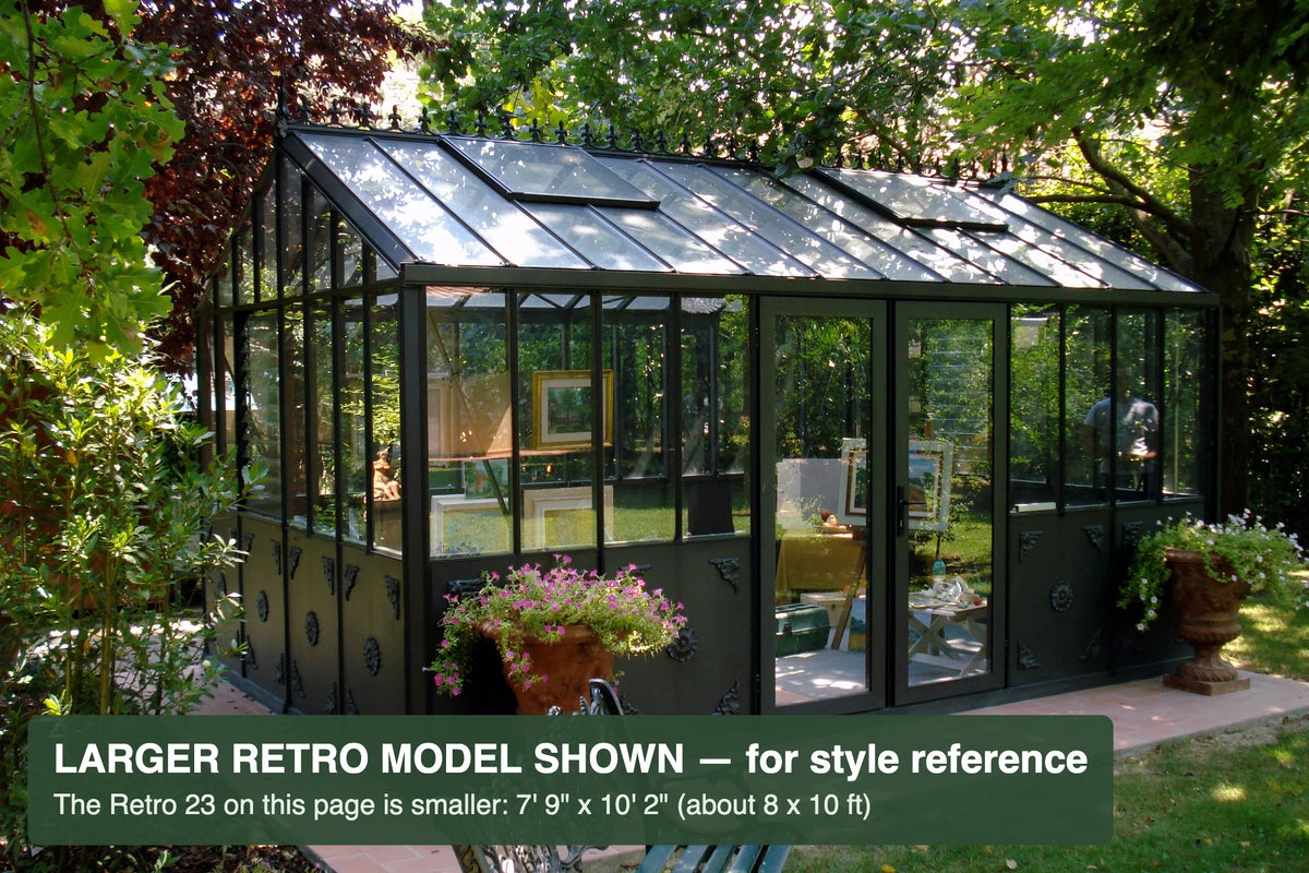 Black Janssens Retro Victorian greenhouse on a tree-lined patio – larger Retro model shown for style reference; the Retro 23 is 7'9" x 10'2"
