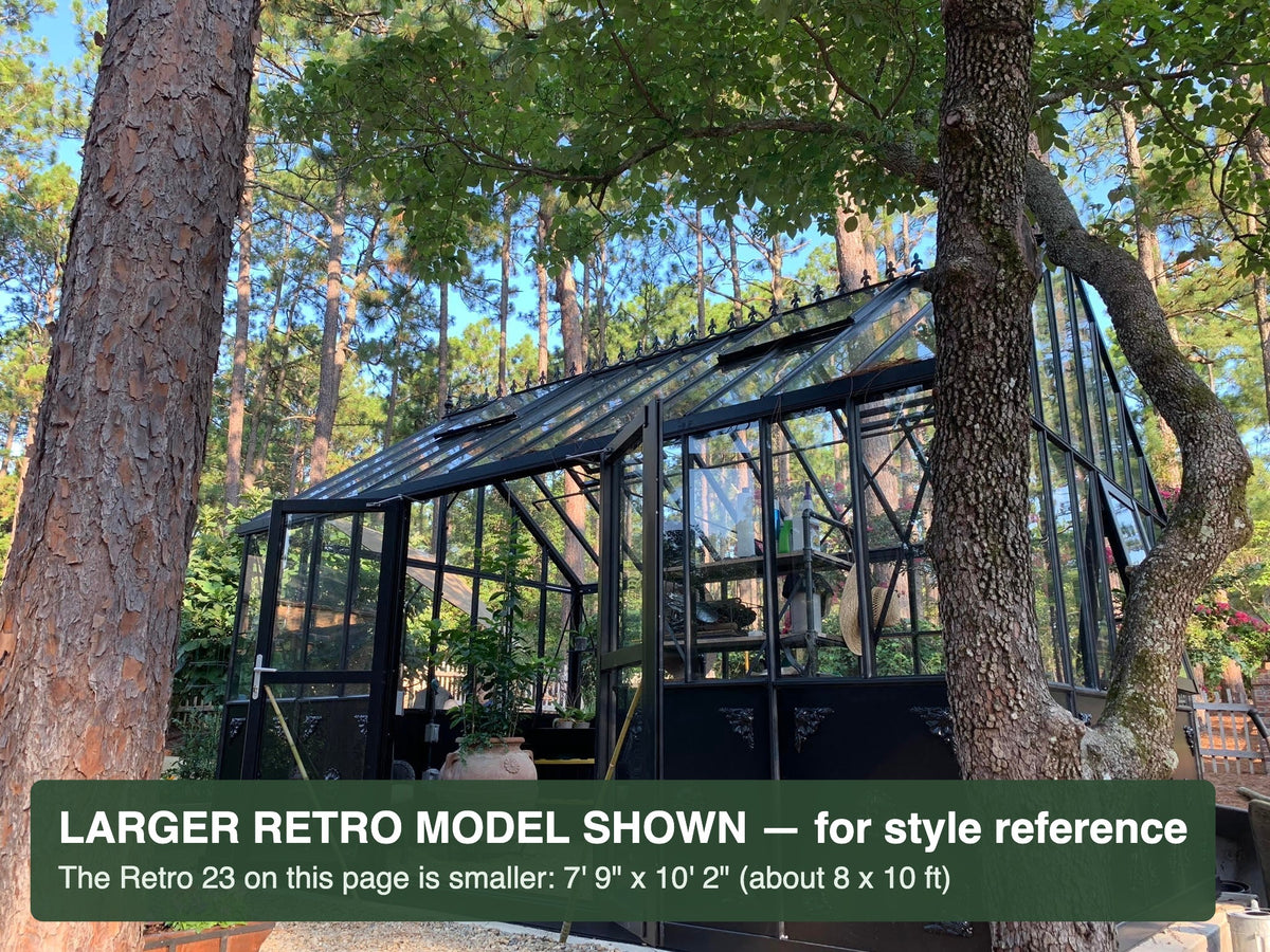 Black Janssens Retro Victorian greenhouse among pine trees – larger Retro model shown for style reference; the Retro 23 is 7'9" x 10'2"