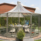 Rondo round glass pavilion with pyramid roof and silver-grey frame on a lawn beside a brick house, set for dining