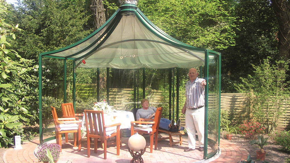 Green-frame Rondo pavilion with pyramid roof and walls rotated open over a patio dining set