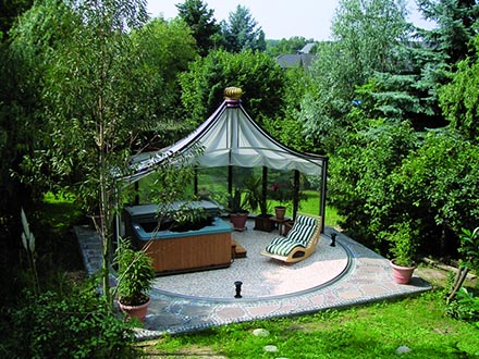 Rondo pavilion covering a hot tub and lounge chair on a round stone patio