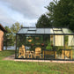 Royal Victorian VI34 greenhouse on a paver base on a lawn, furnished with wooden chairs and plants