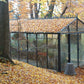 Royal Victorian VI36 greenhouse in autumn, its roof covered in fallen leaves on a wooded slope