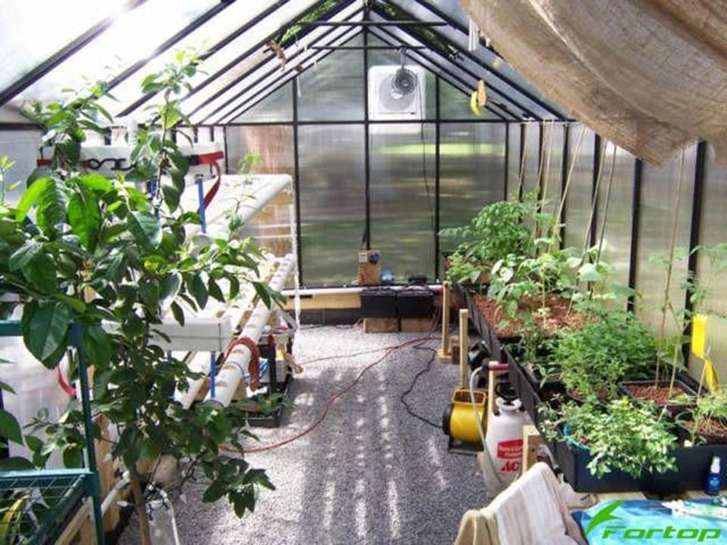 Inside a long Riverstone MONT greenhouse with potted plants, shade cloth and a gravel floor