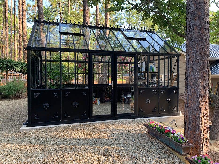 Black Retro Royal Victorian VI34 glass greenhouse on a patio under trees