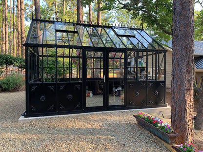 Black Retro Royal Victorian VI34 glass greenhouse on a patio under trees
